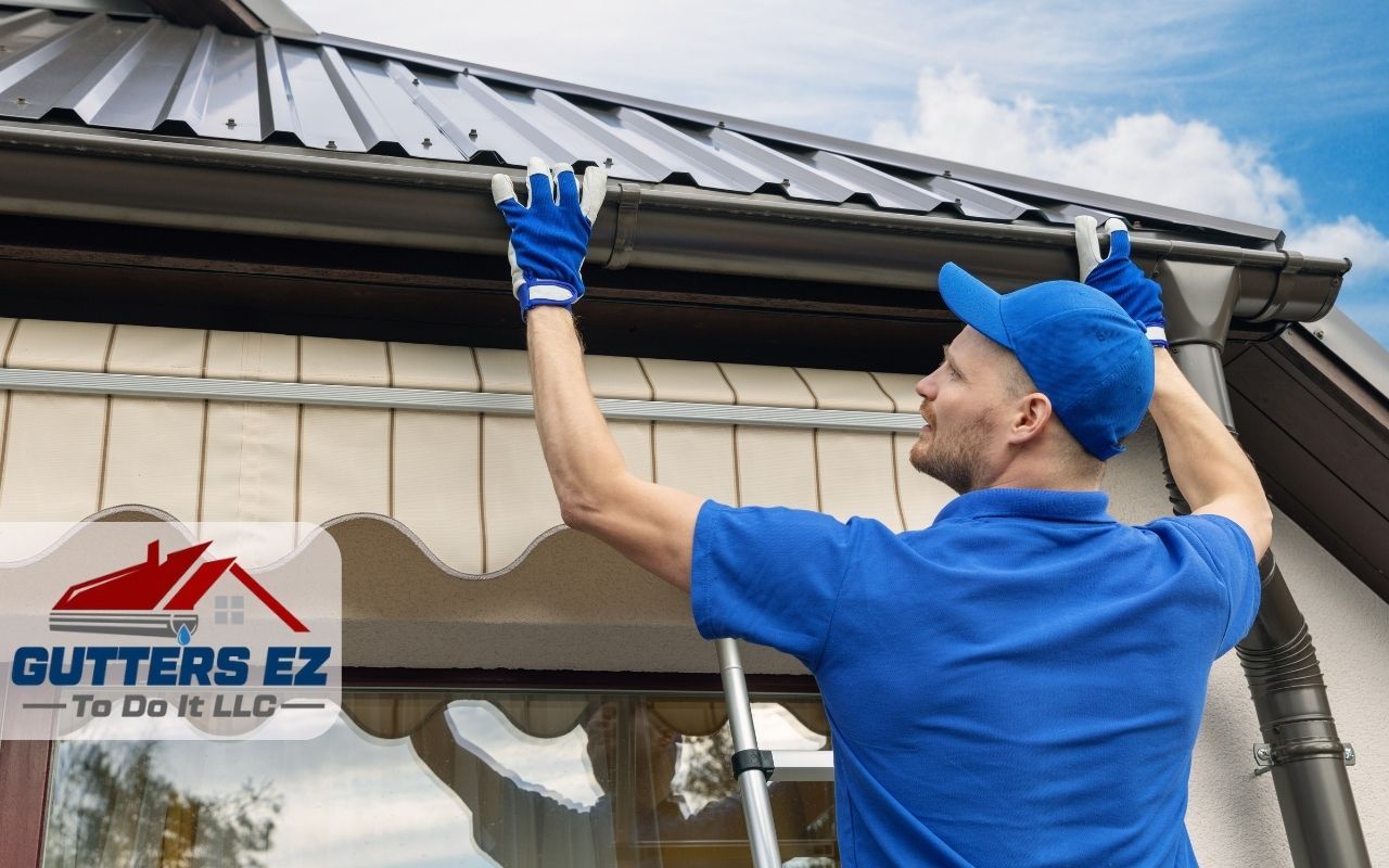 Worker in blue uniform inspecting and cleaning a gutter on a house roof edge