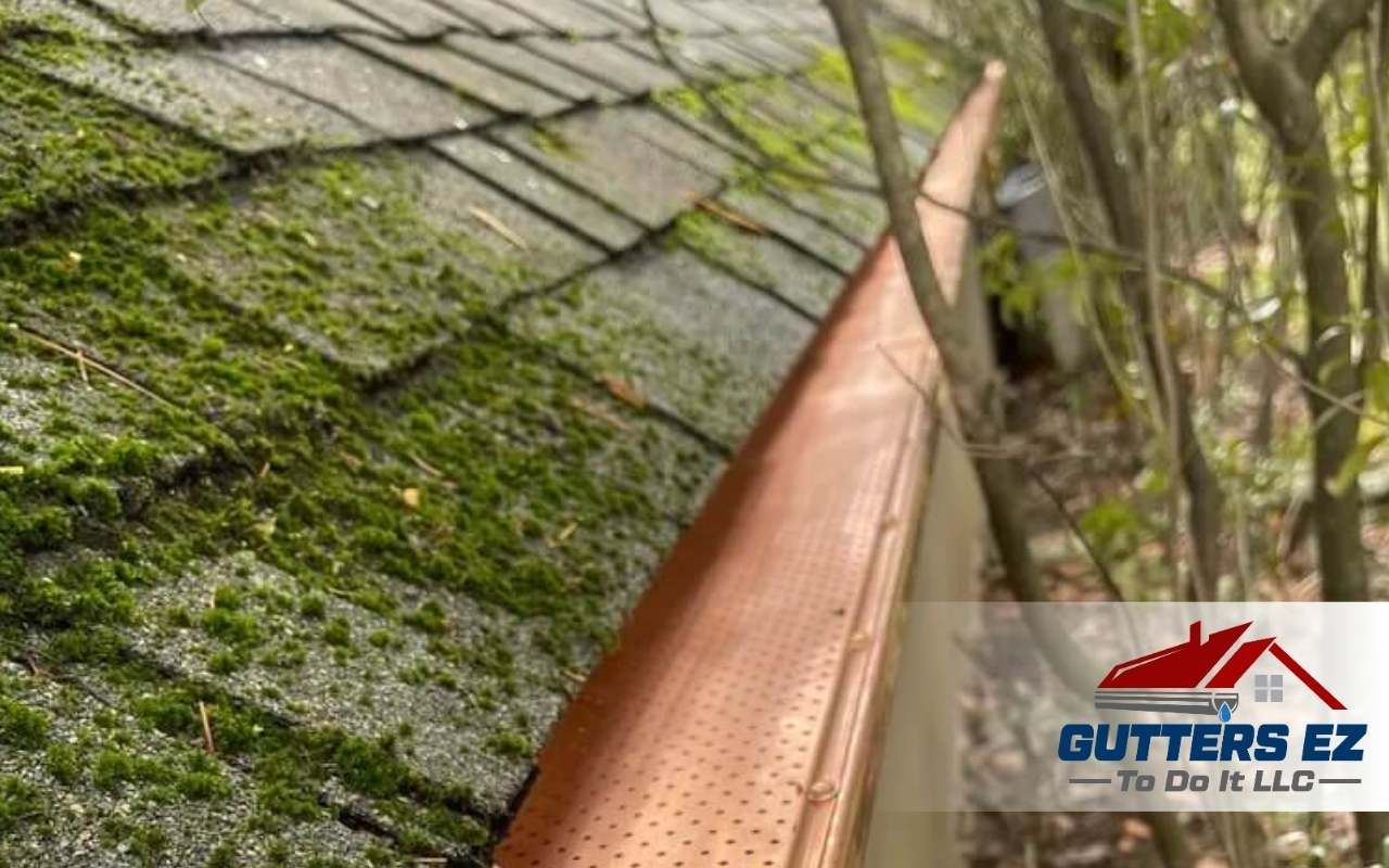 Gutter cleaning on a mossy roof beside a copper-colored gutter and tree branches