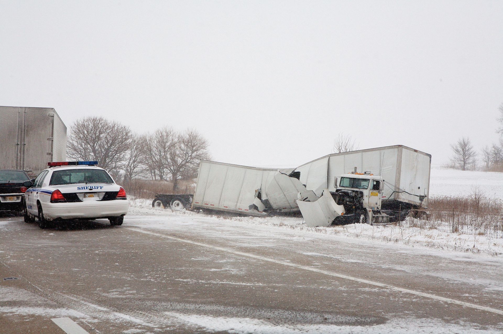 A damaged semi-truck on a snow-covered road with a police car present.