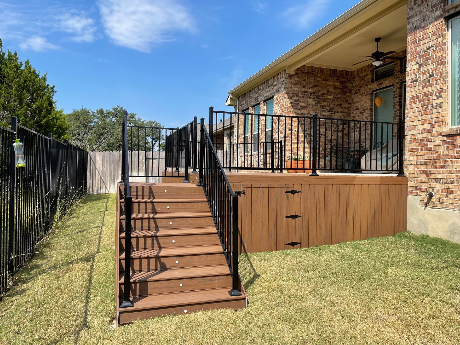 A wooden deck with stairs leading up to it is in the backyard of a house.