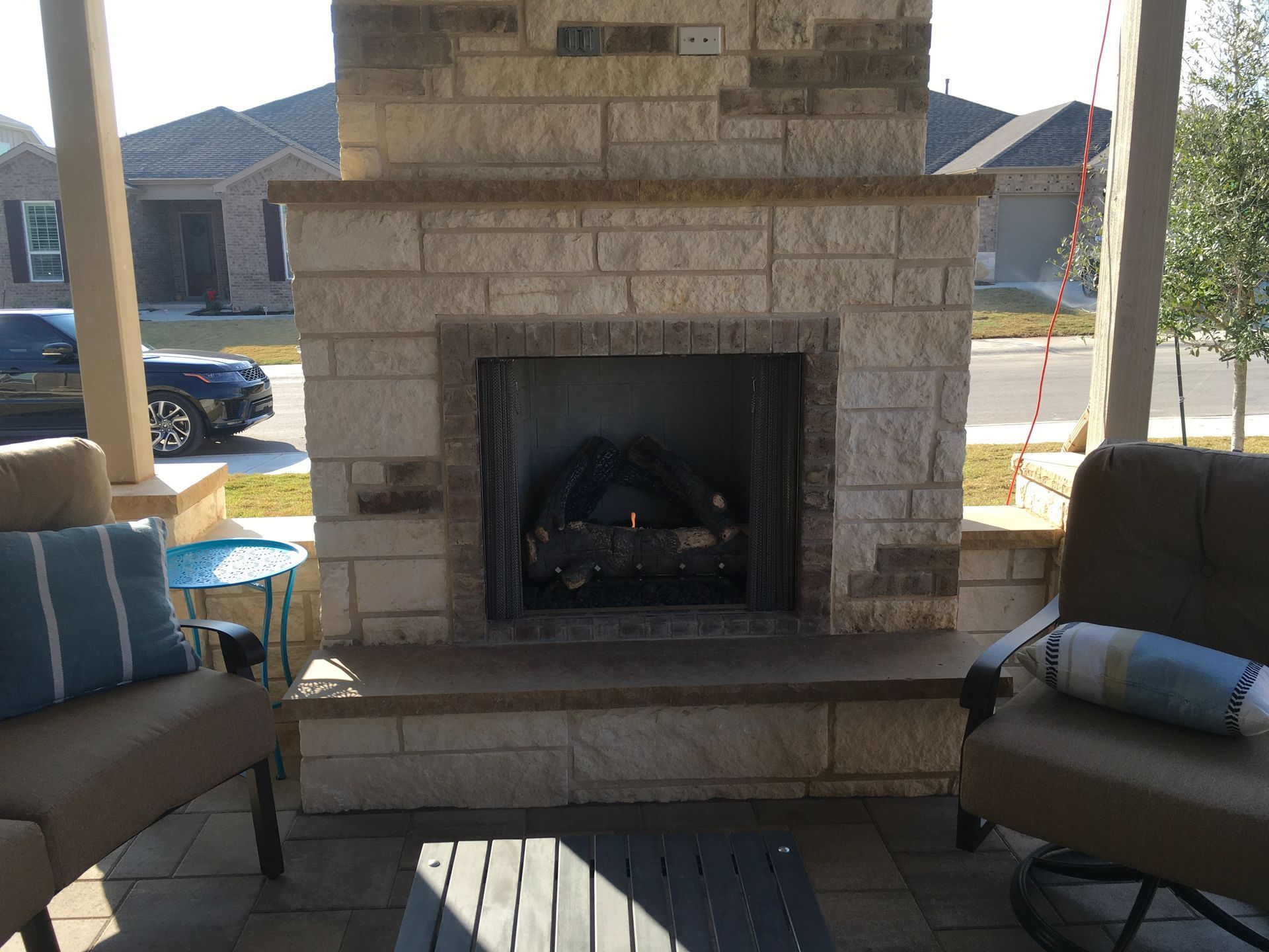 A brick fireplace is sitting on a porch next to a couch and chairs.