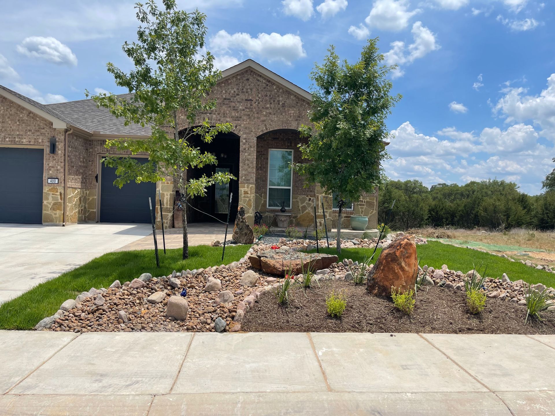 A brick house with a lush green lawn and a rock garden in front of it.