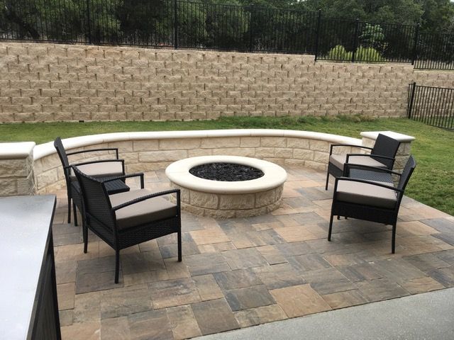 A fire pit on a patio with chairs and a brick wall.