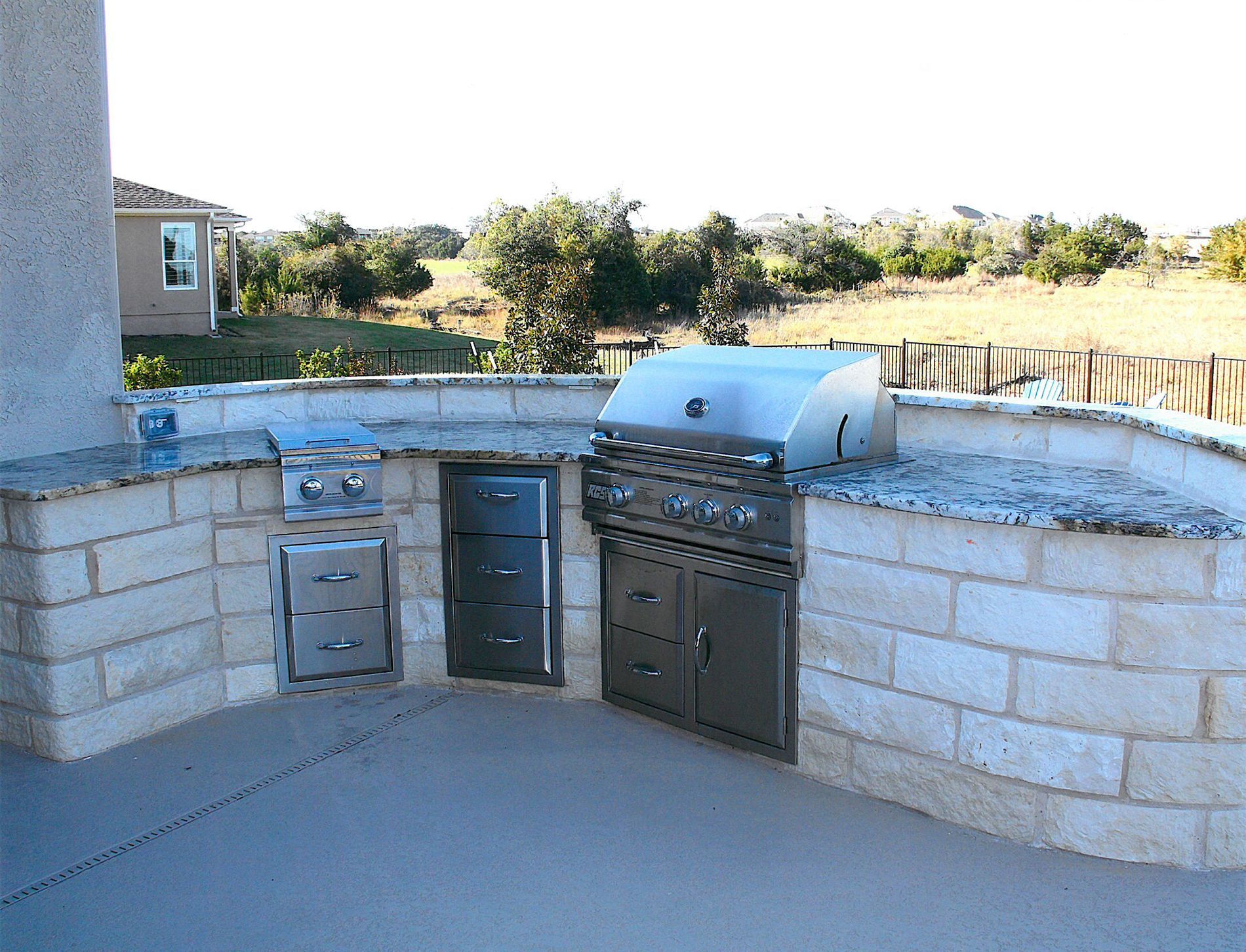 An outdoor kitchen with a stainless steel grill and granite counter tops