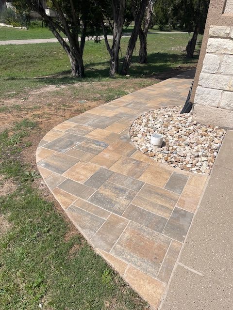 A brick walkway leading to a house with trees in the background.