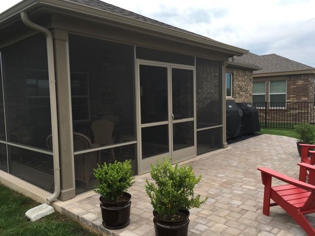A screened in porch with red chairs and potted plants