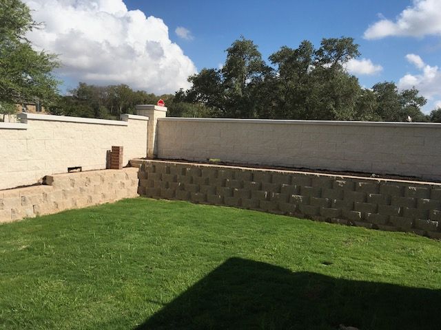 A backyard with a brick wall and a lush green lawn