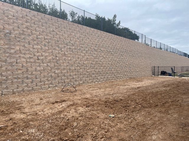 A large brick wall surrounds a dirt field with a fence in the background.