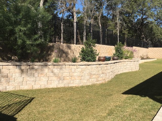 A brick wall surrounds a lush green lawn in a backyard.