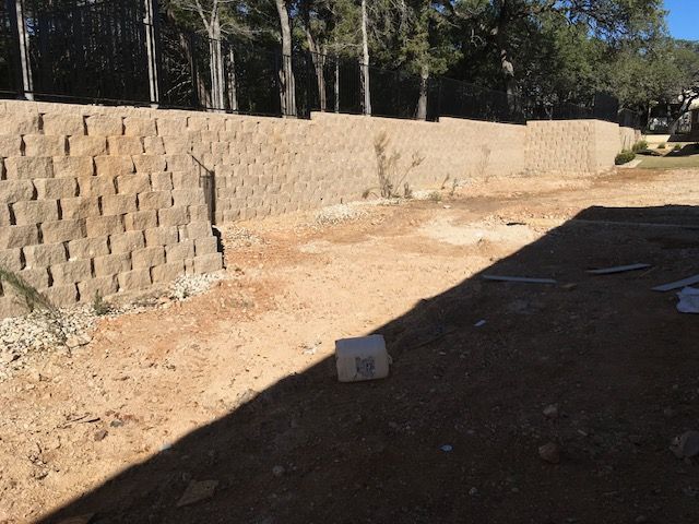 A large brick wall is surrounded by dirt and trees