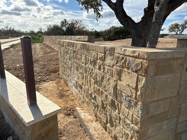 A stone wall with a tree in the background is being built.