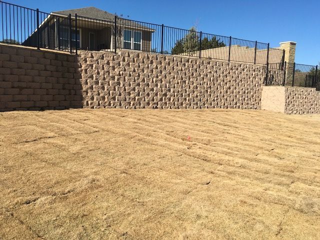 A large brick wall surrounds a lush green field in front of a house.