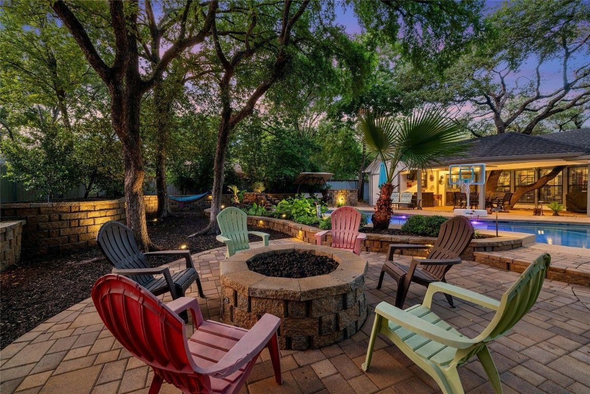 A fire pit surrounded by chairs on a patio next to a pool.
