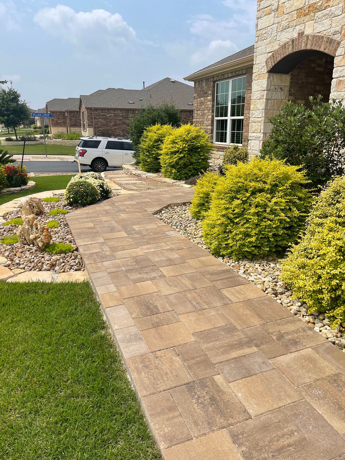 A walkway leading to a house with a car parked on the side of it.