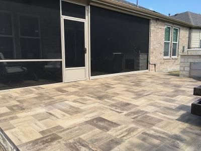 A patio with a screened in porch and a brick house in the background.
