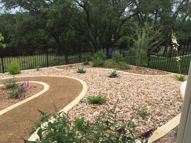 A garden with a fence , gravel , plants and trees.