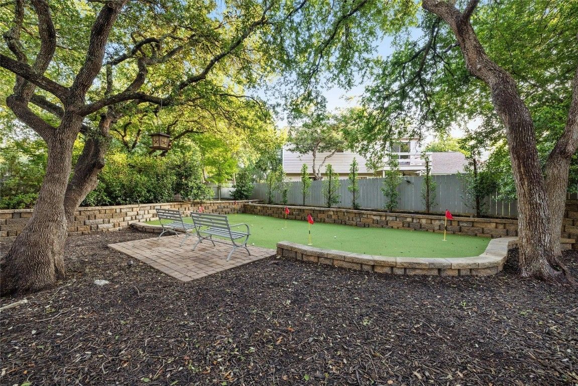 There is a putting green in the backyard surrounded by trees.