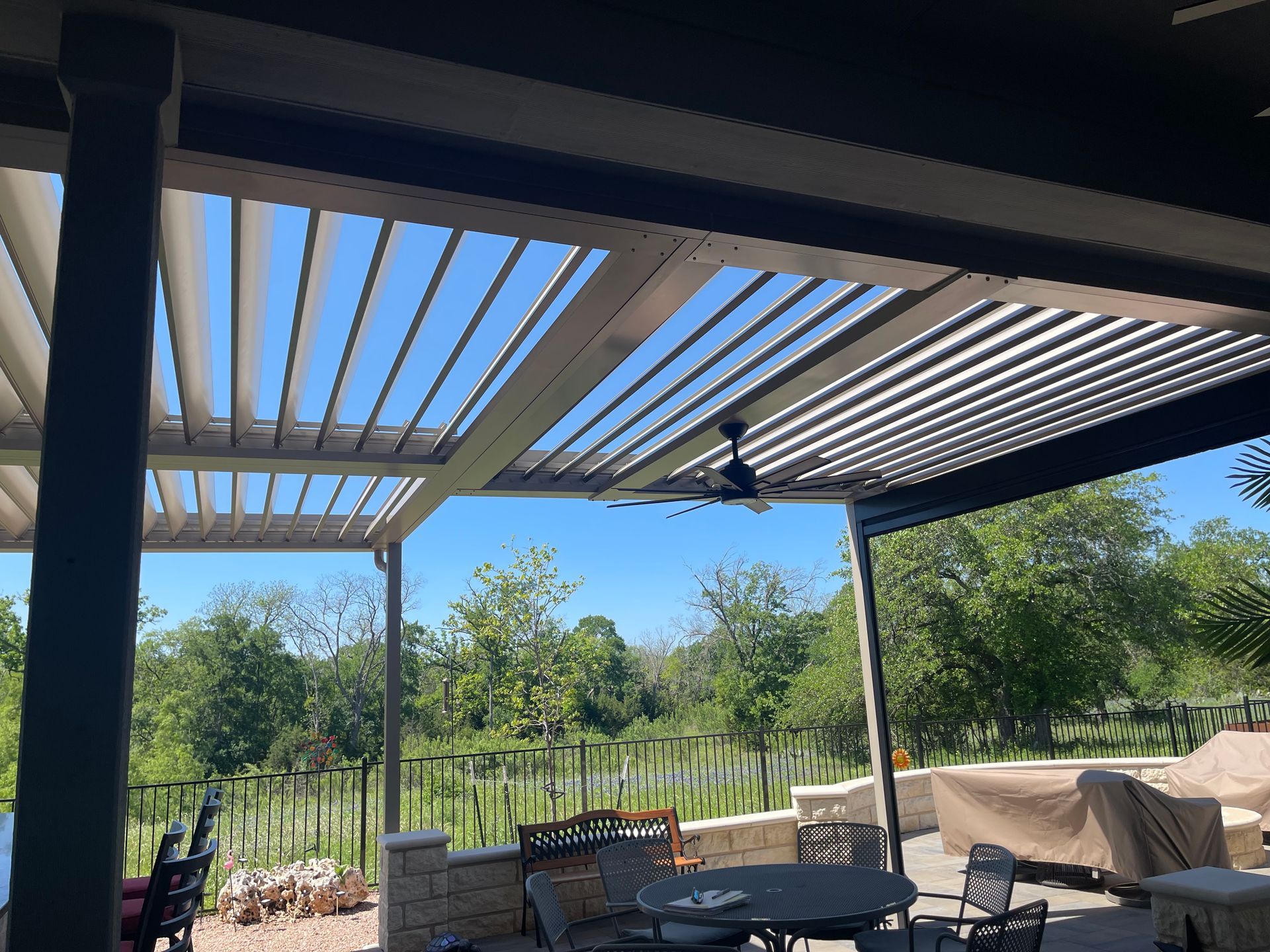 A patio with a table and chairs under a pergola with a ceiling fan.