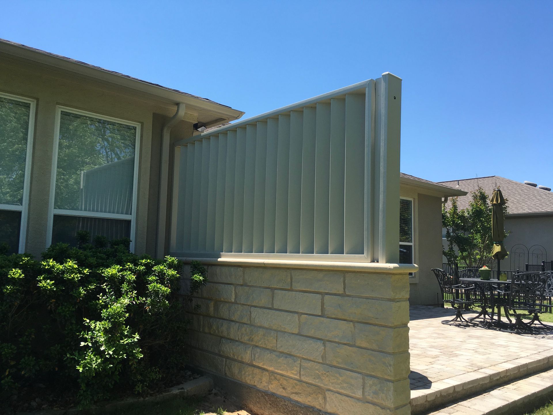 A white fence is sitting next to a brick wall in front of a house.