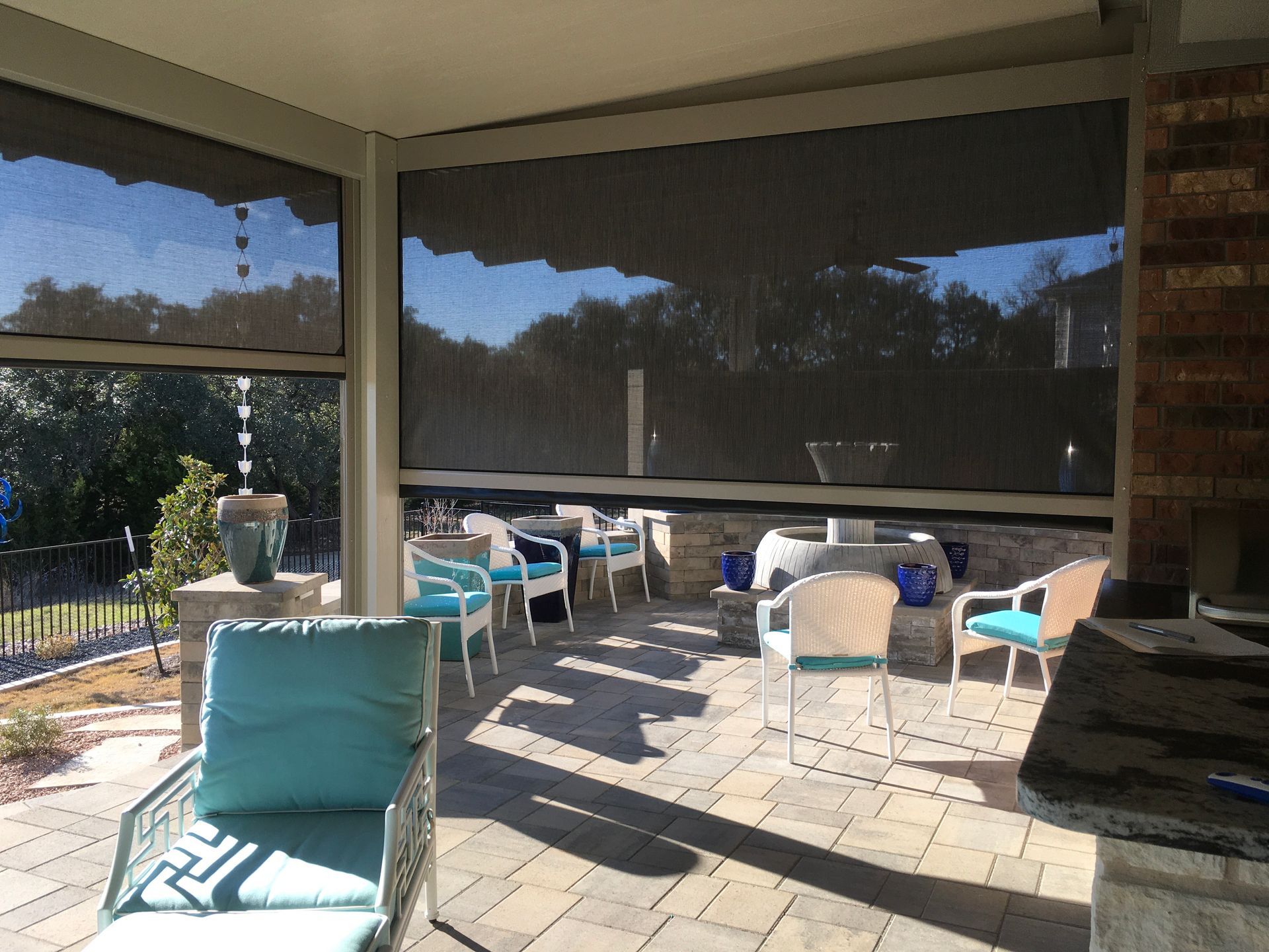 A screened in porch with chairs, tables and a fireplace.