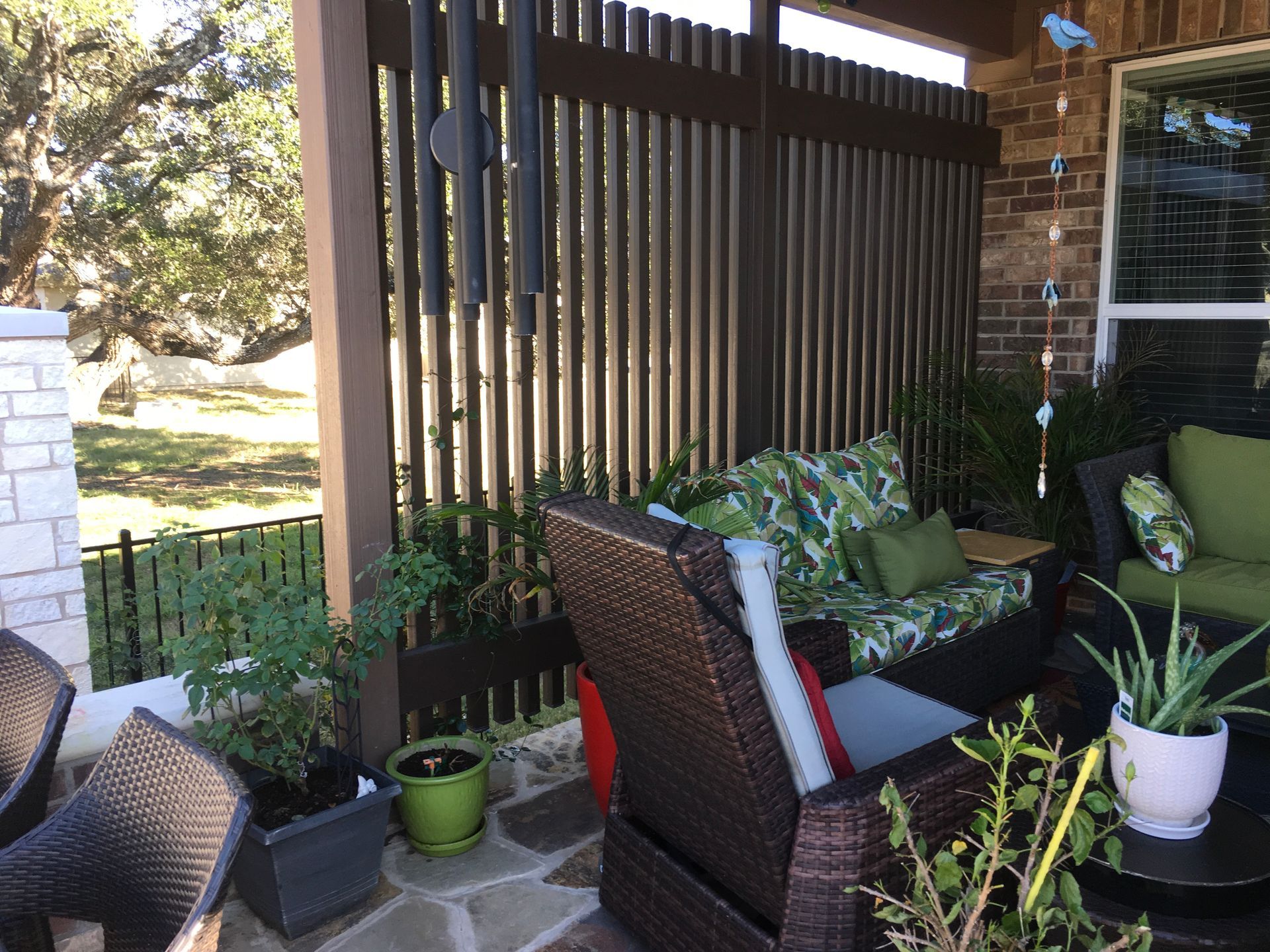 A patio with a wicker chair, couch, table and potted plants.