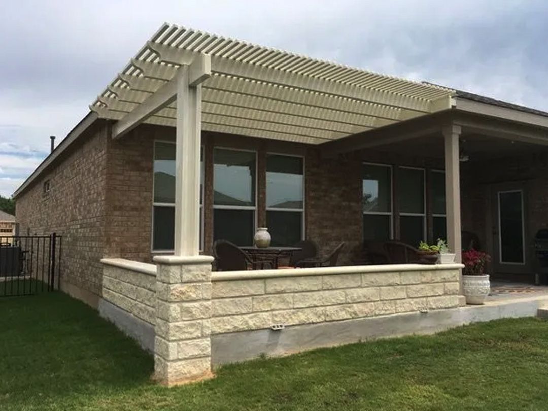 Brick home with beige pergola and stone retaining wall over a patio with grass.