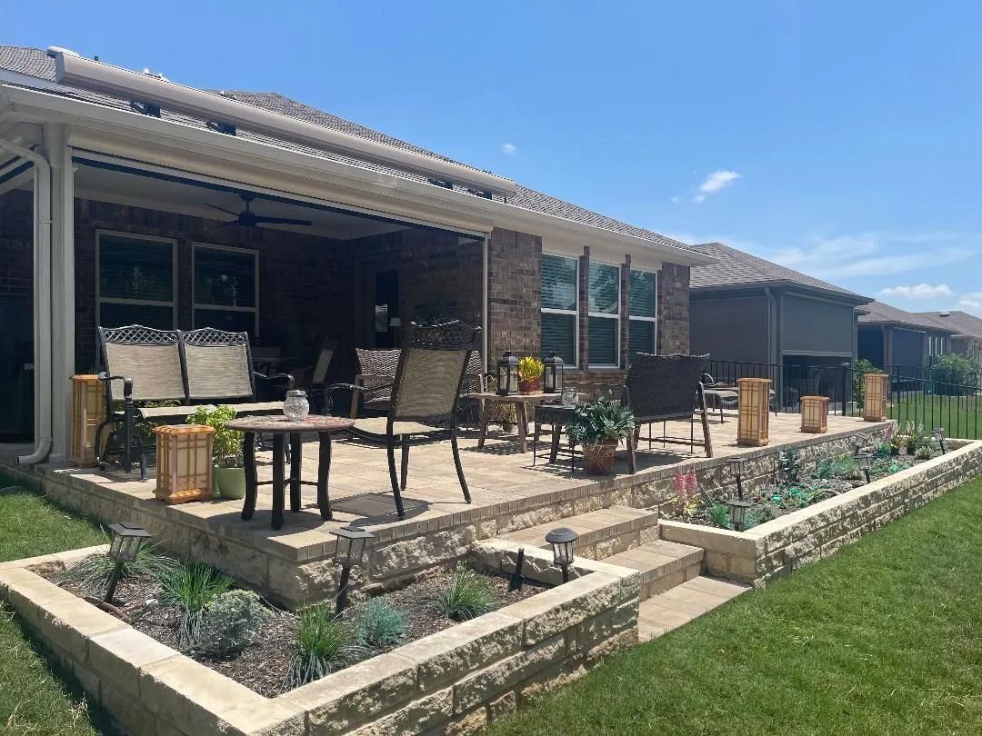 Patio with seating, planters, and raised beds, with a brick house under a blue sky.