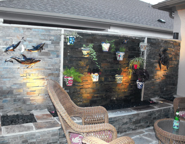 A patio with chairs and a table in front of a wall with potted plants on it