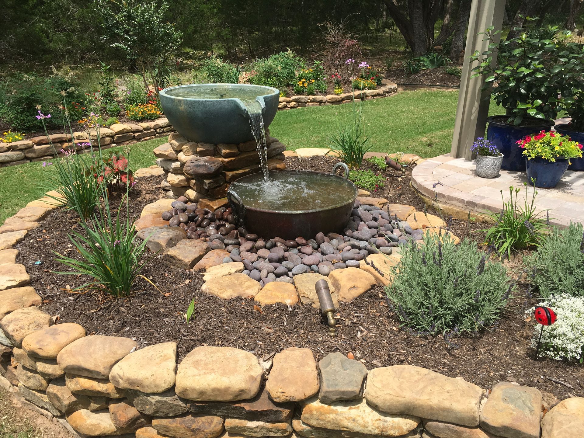 A water fountain in a garden surrounded by rocks and flowers.
