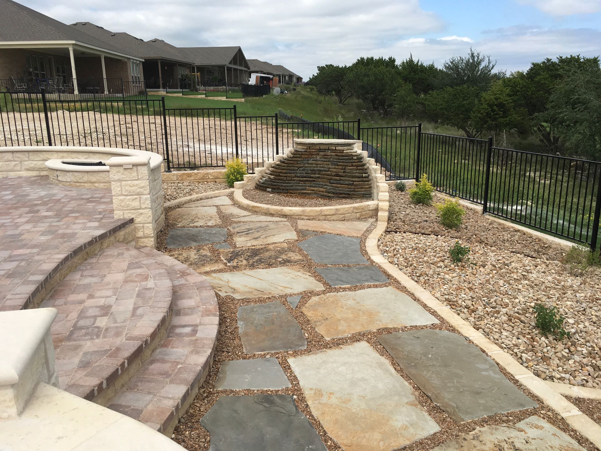 A stone walkway leading to a house with a fence in the background