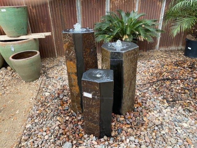 A fountain is sitting on top of a pile of gravel next to a potted plant.