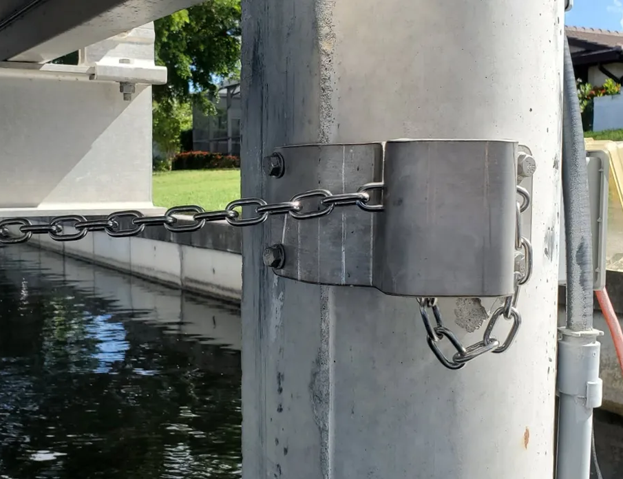 Silver chain and brackets secured to a gray concrete post, possibly part of a dock or pier over water.