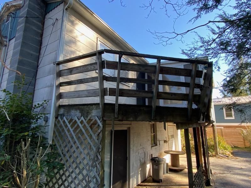 Wooden deck with railing attached to a white building, with a concrete chimney and an open door below.
