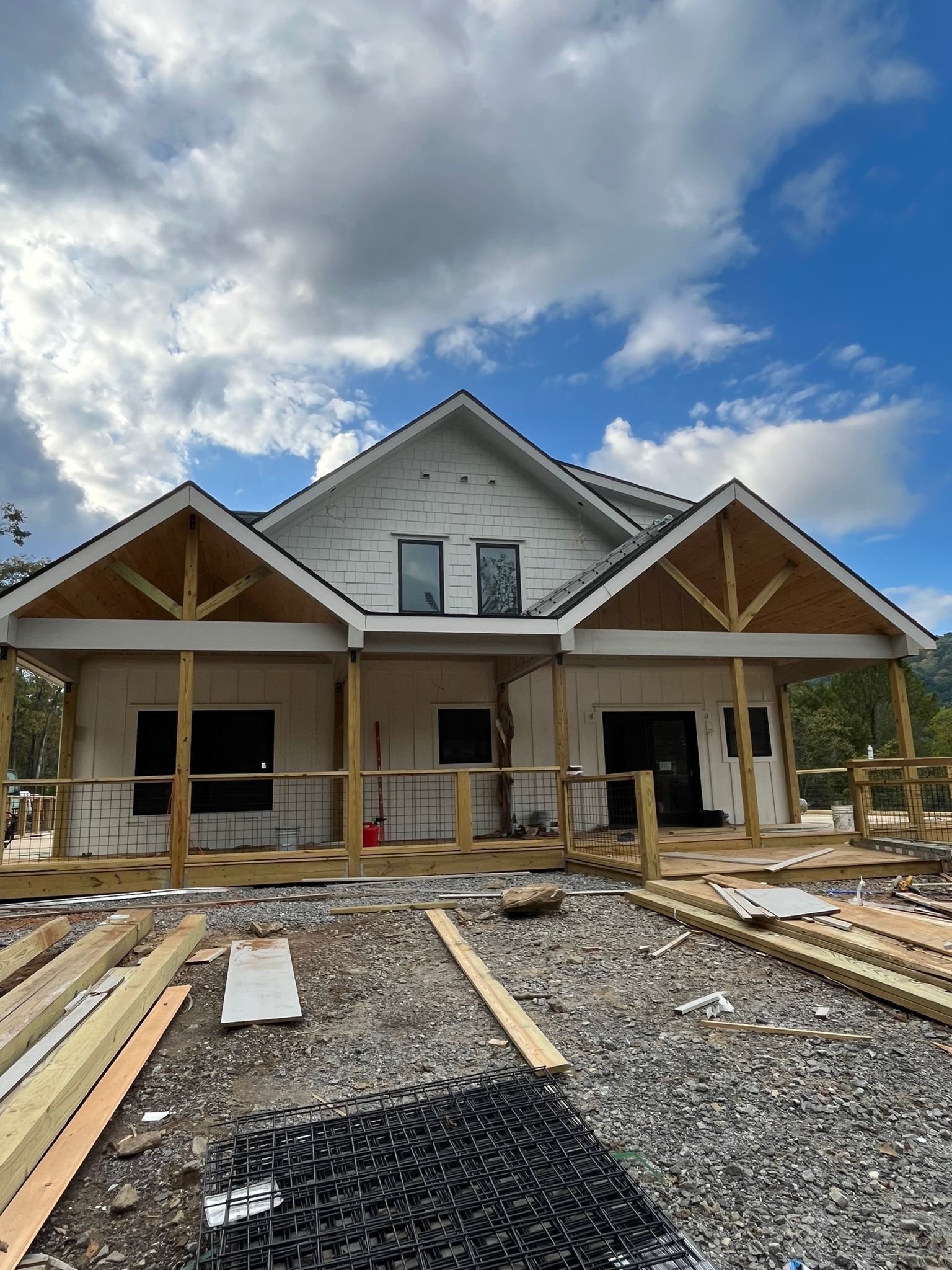 House under construction with porch, wood framing, and siding against a cloudy sky.