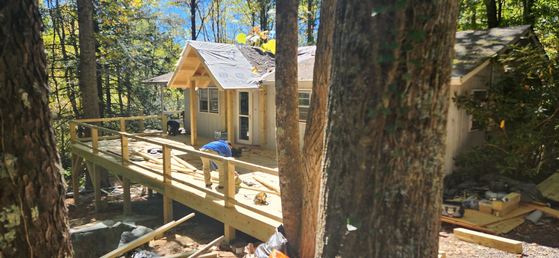 Cabin under construction in a forest, featuring a wooden deck and a view of the surrounding trees.