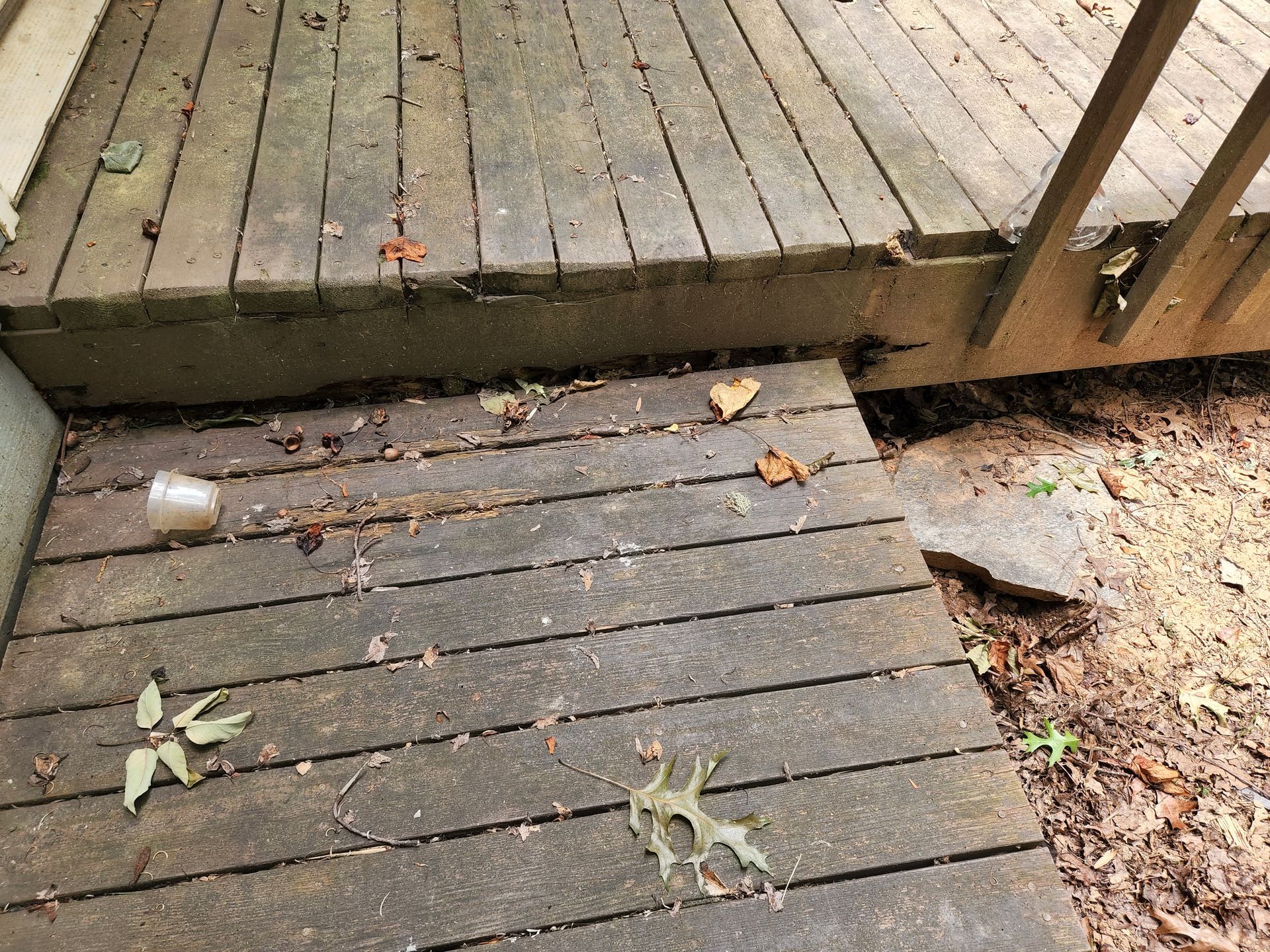 Wooden deck with cracks and debris, connecting to uneven ground.