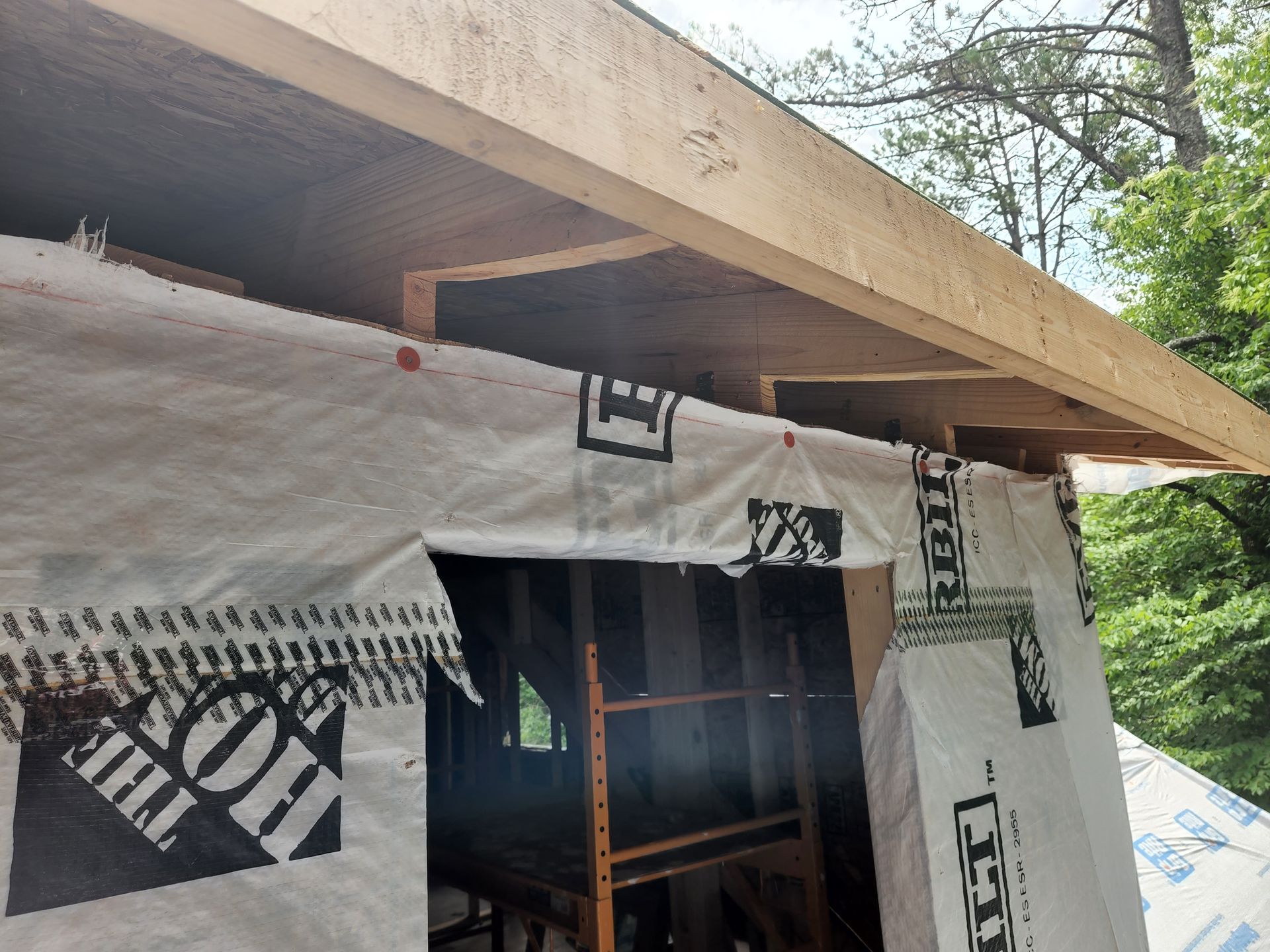 Building exterior with wood frame, white tarp, and part of a roof.