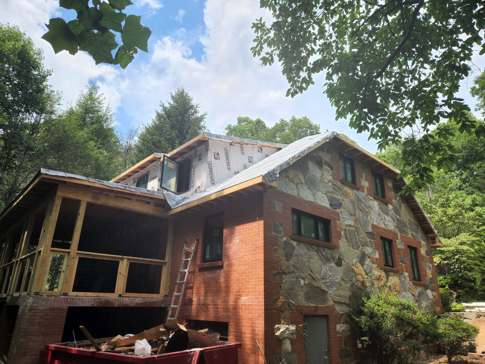 House under construction with stone facade and new roofing; porch is being built.