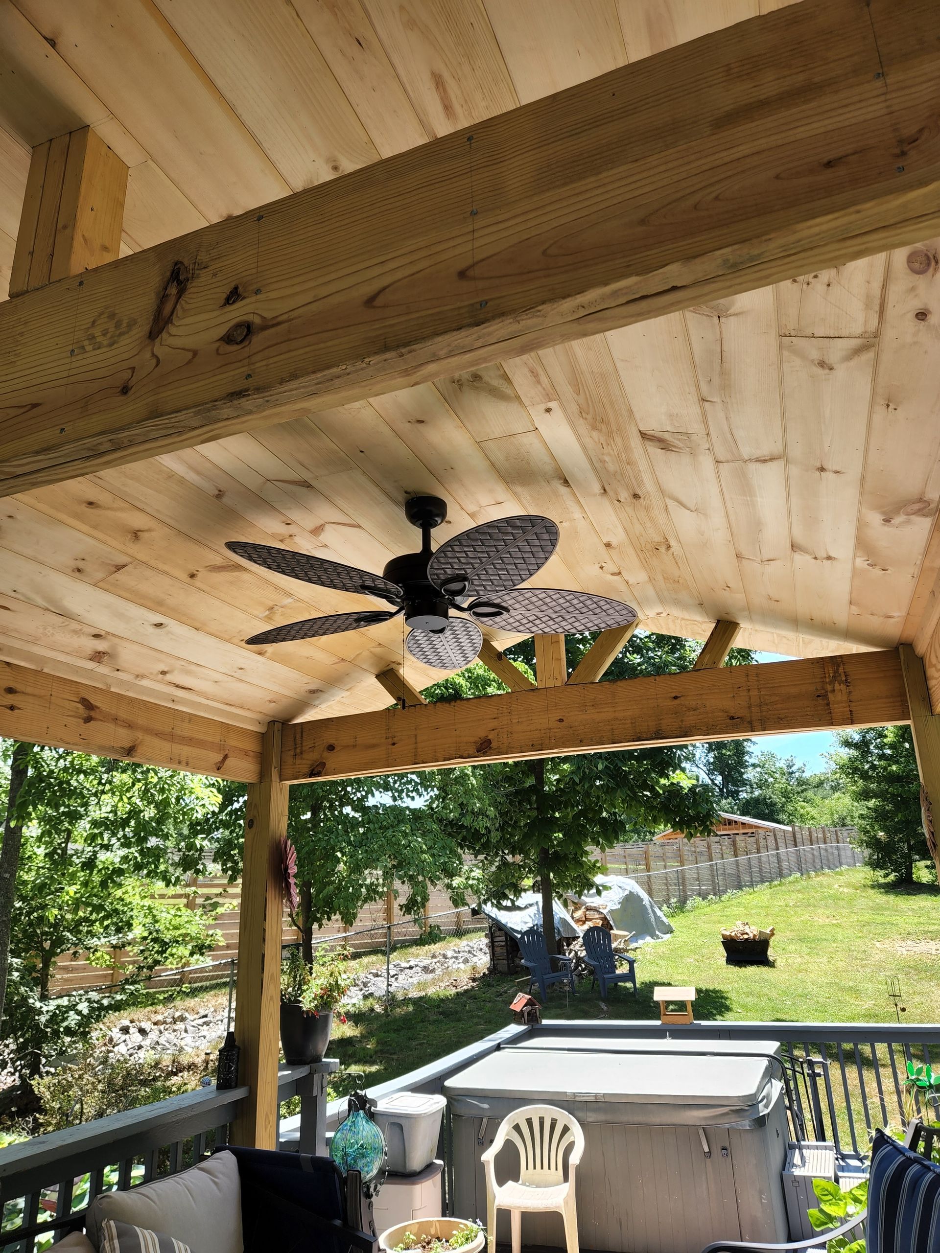 Covered porch with wood ceiling, ceiling fan, and view of yard and trees.