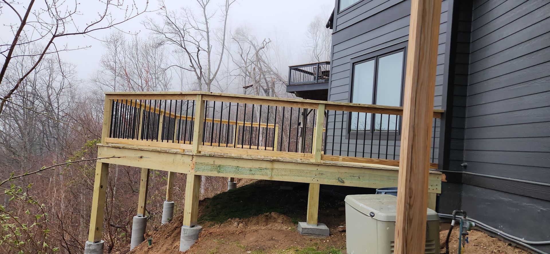 Wooden deck attached to a gray house with a metal railing, overlooking a foggy landscape.
