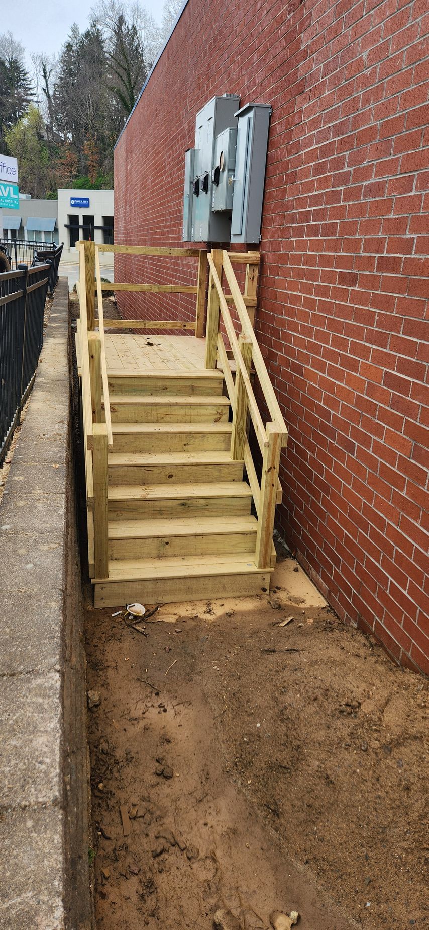 Wooden stairs with railings against a brick wall, leading up to electrical boxes.