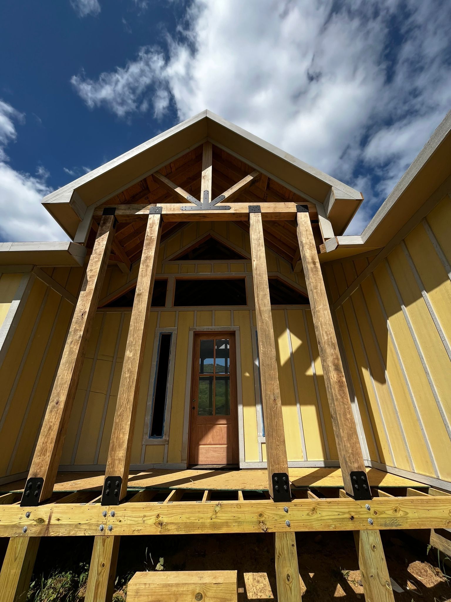 Wooden house under construction, featuring a front door, porch, and roof.