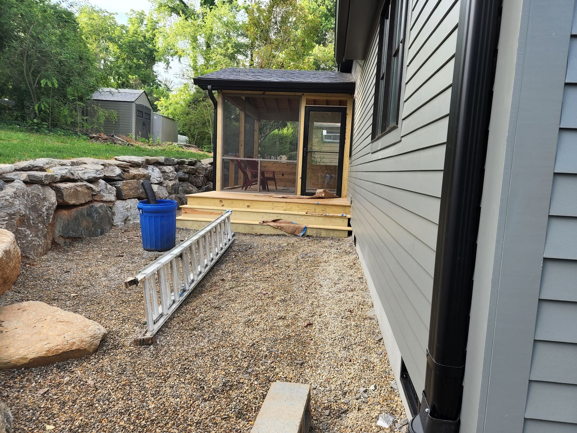 Side view of a house with light blue siding and a screened porch on a gravel patio.