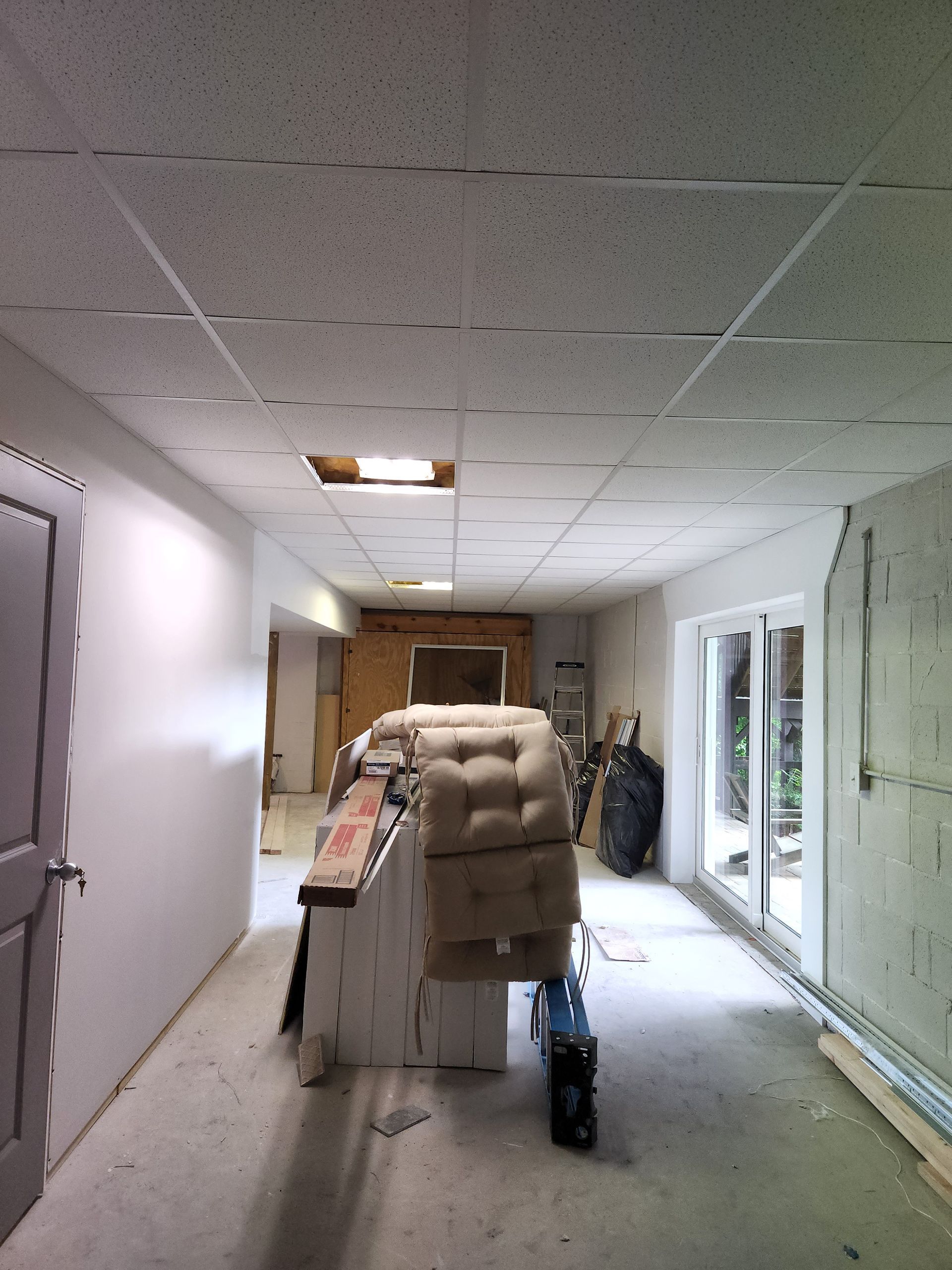 Hallway under construction with unfinished walls, a drop ceiling, and construction materials.