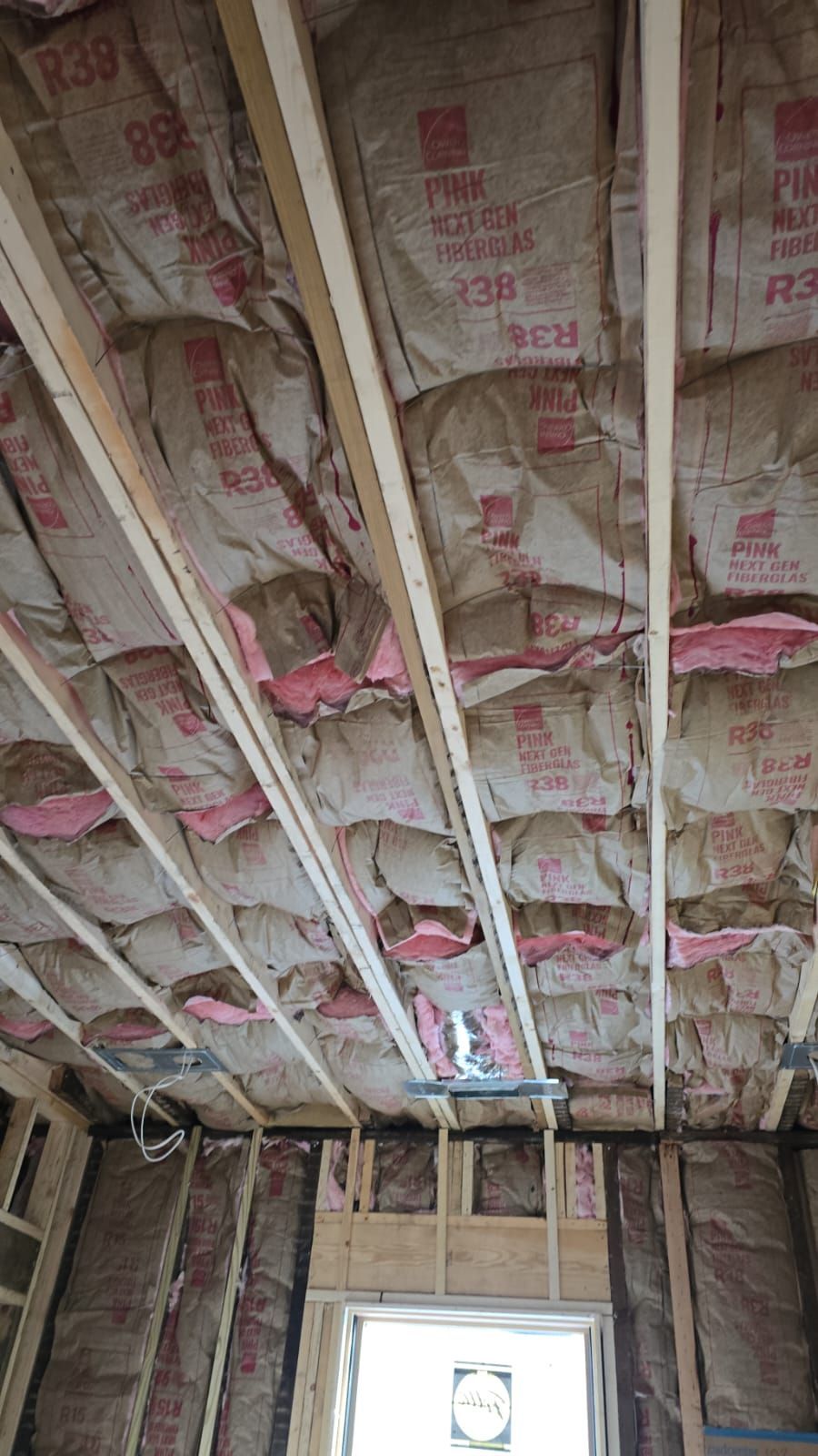 Unfinished room with exposed wooden beams and pink insulation. Wall studs visible around a doorway.
