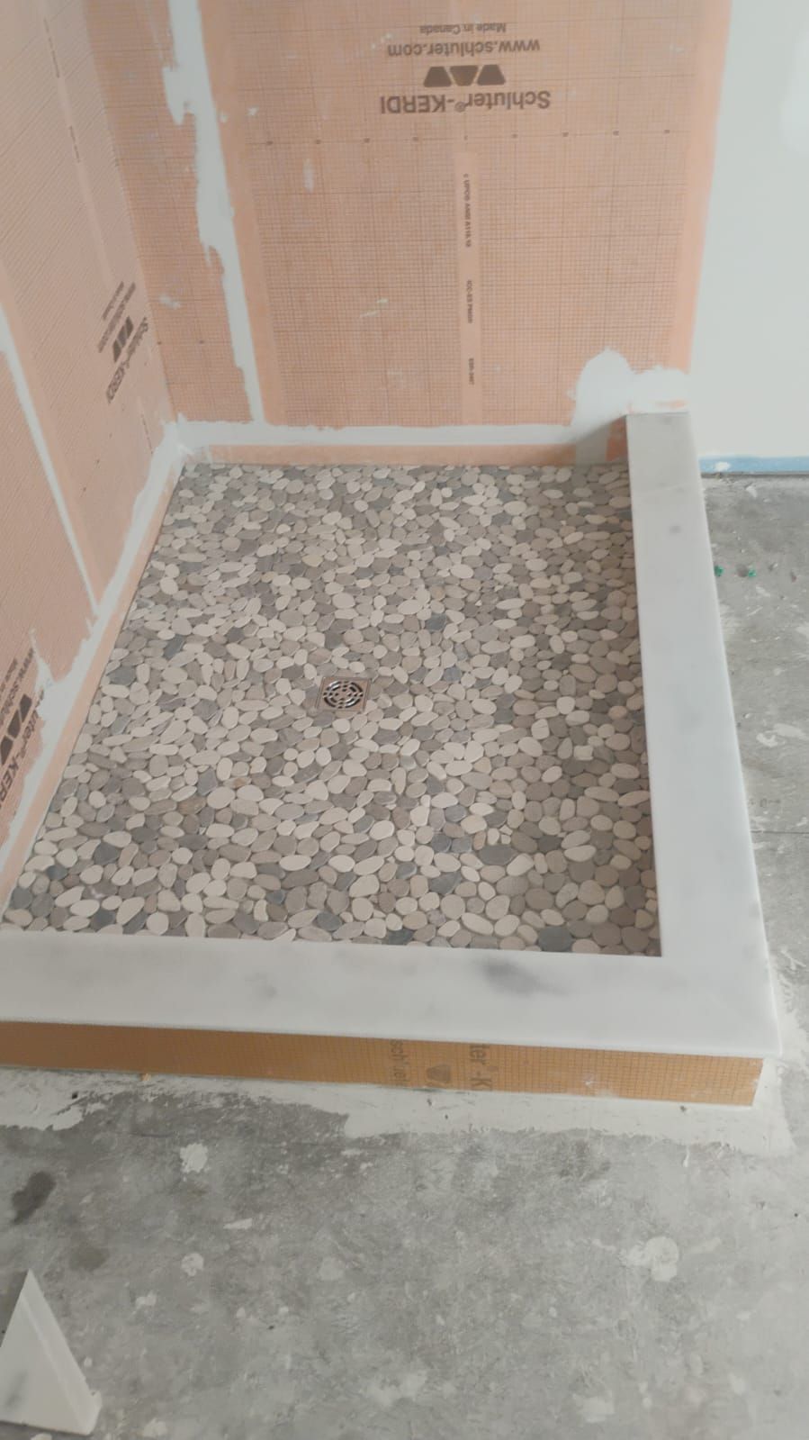 Shower floor with stone tile and concrete curb. Walls have waterproofing membrane.