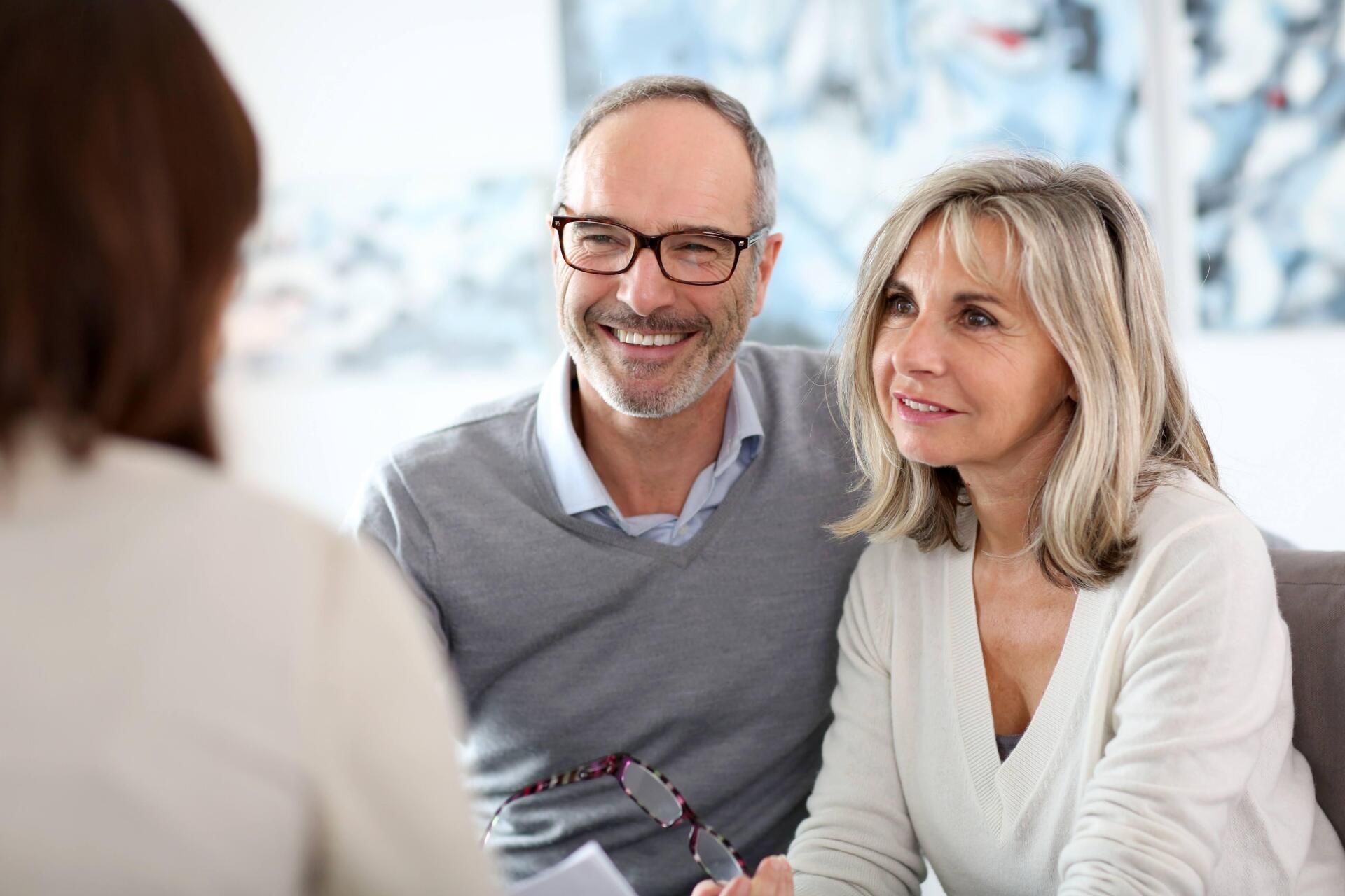 Couple smiles while consulting with a person. They sit on a couch in an office.