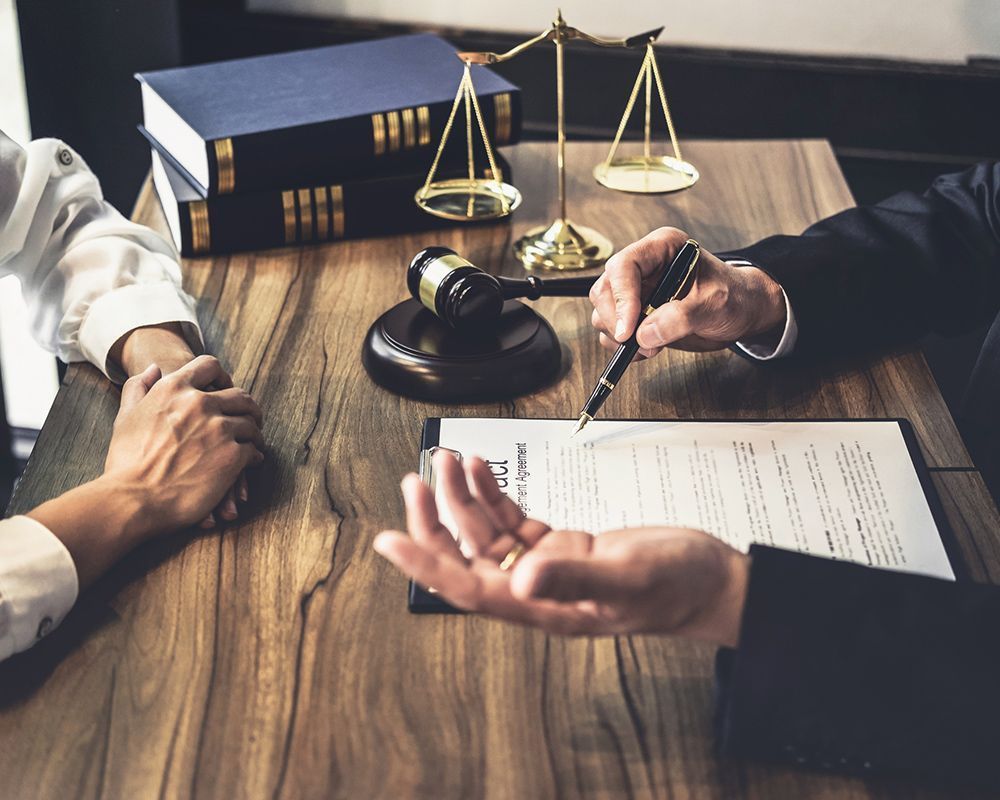 Lawyer points to document, explaining to a client at a wooden desk with law books, gavel, and scales.