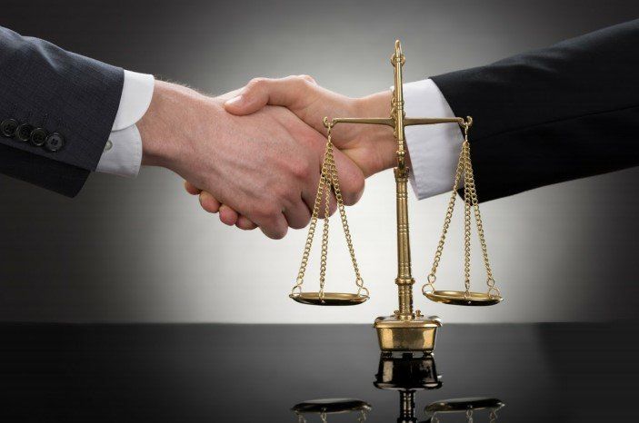Two people shaking hands with a justice scale in between them.
