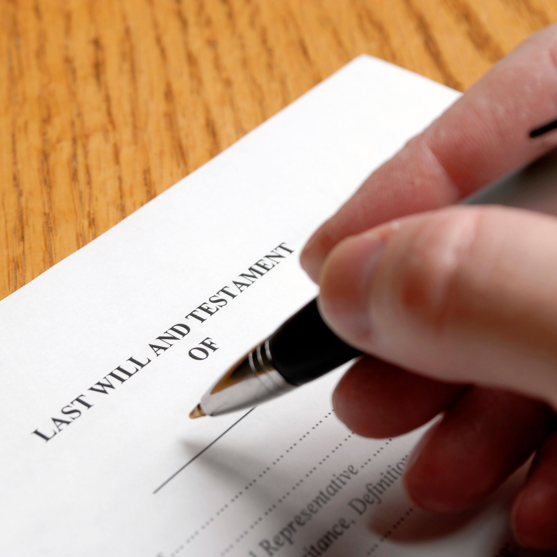 Hand signing a Last Will and Testament document with a pen on a wooden surface.
